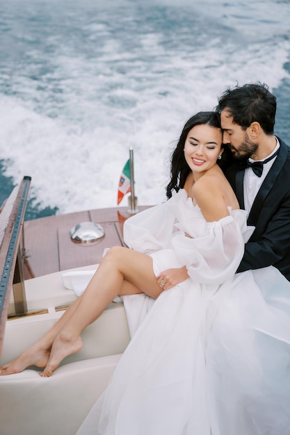 Groom hugs bride from behind touching foreheads on a yacht sailing on the sea