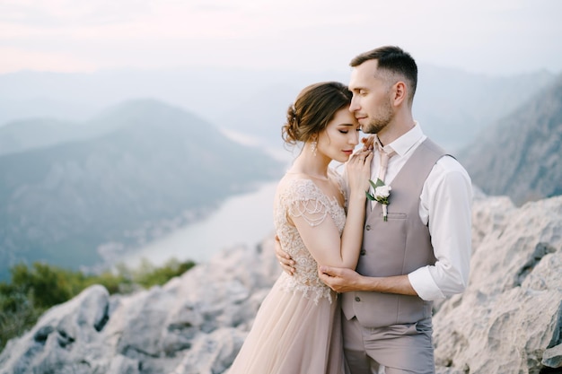 Groom hugs bride on the mountain on the background of kotor bay