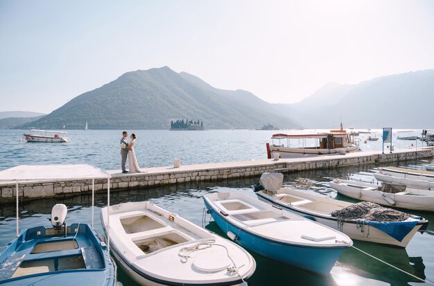 Groom hugs bride on the pier against the background of parked boats