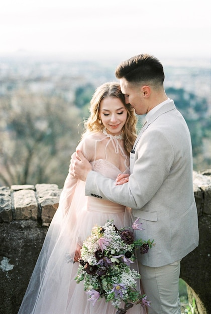 Groom hugs bride with a bouquet on the roof of the house bergamo italy