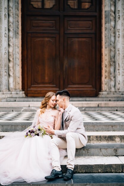 Groom hugs and kisses bride at the entrance to the basilica of santa maria