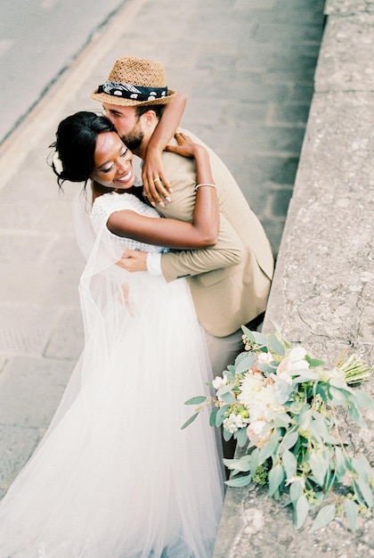 Groom hugs and kisses bride near the stone fence top view