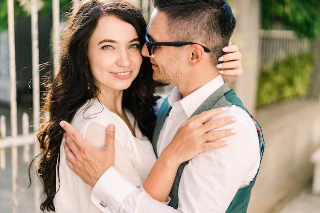 Groom hugs the shoulders of smiling bride touching his hair with her hands