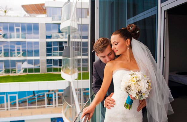 Lo sposo tiene in braccio una bella sposa e la bacia sul balcone