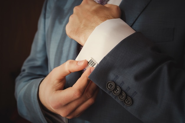 Groom is putting on cuff-links as he gets dressed in formal wear close up