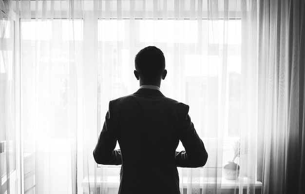 Groom is standing near the window wedding day black and white photo