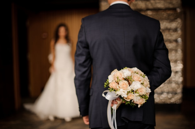 Groom keeping behind a bouquet of roses waiting for bride