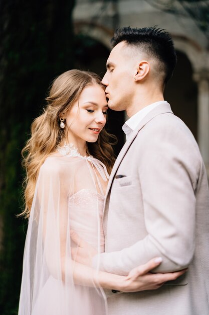 Lo sposo bacia la fronte della sposa sorridente in un bellissimo vestito rosa