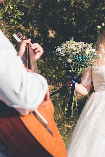 Groom plays the guitar, bride holds a wedding bouquet. Vertical orientation, no faces.