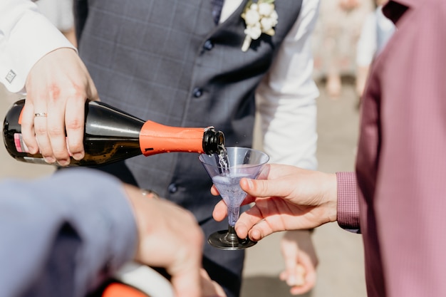 Lo sposo versa lo champagne in un bicchiere di plastica per il primo piano degli ospiti.