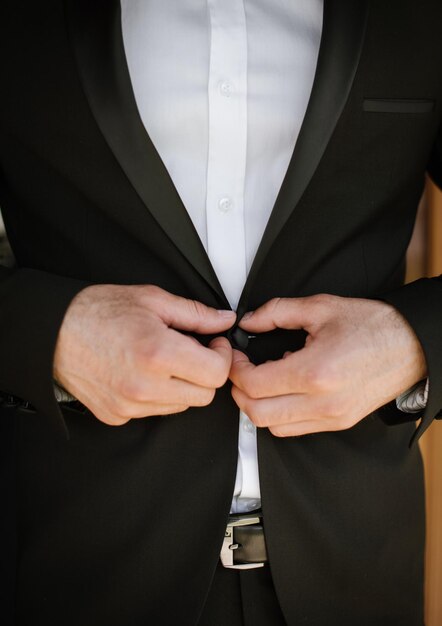 The groom puts on a jacket fastens a button closeup view