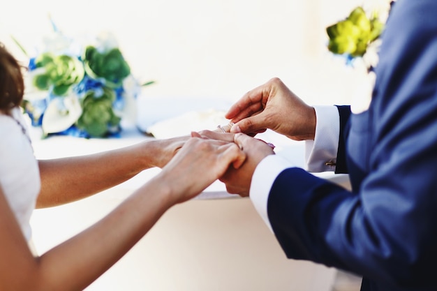 Lo sposo mette un anello sul dito della sposa in piedi sulla spiaggia