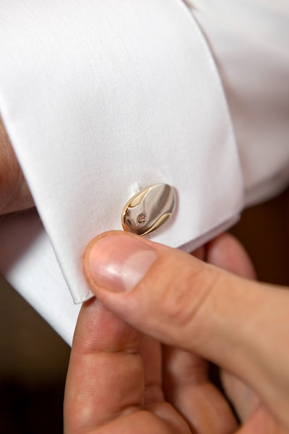 Groom putting on cuff-links as he gets dressed in formal wear close up