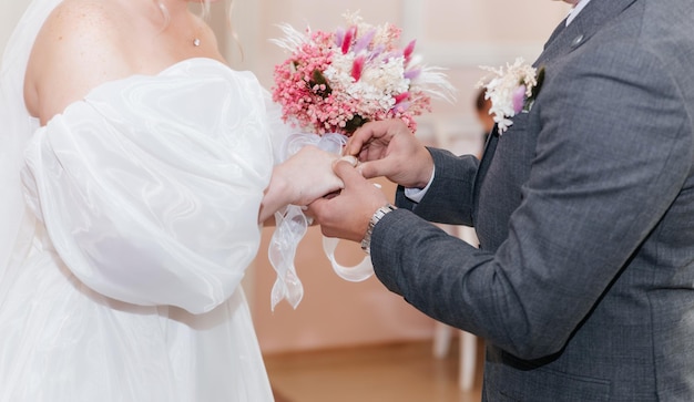 Groom putting golden ring on bride's finger during wedding ceremony Hands with rings close up