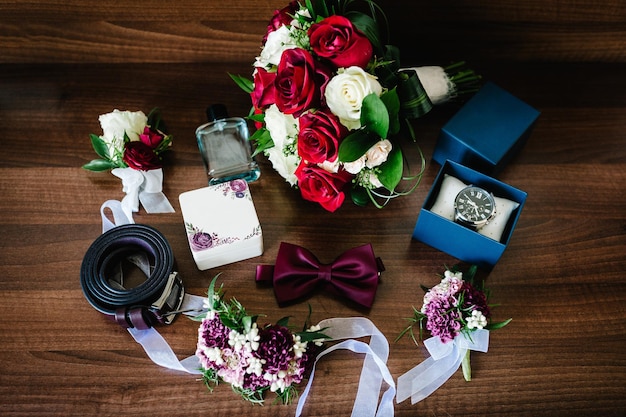 Groom's accessories watch perfume tiebow belt flowers on a wooden brown background