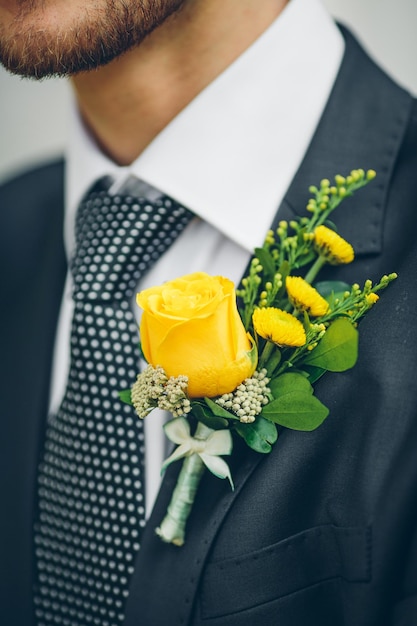 Groom's hand arranging yellow boutonniere flower on suit