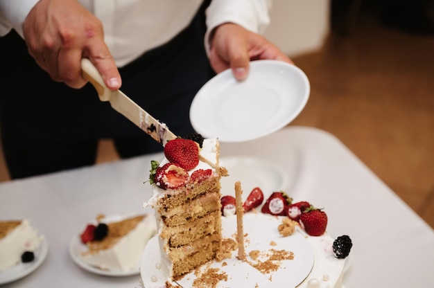 Рука жениха режет свадебный торт на кусочки