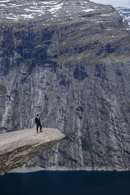 Photo groom standing on a fragment of rock in the mountains, against the background of the fjord