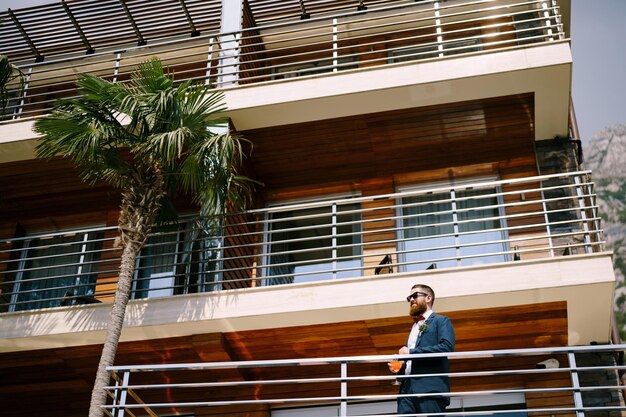 Lo sposo sta sul balcone dell'hotel con un bicchiere in mano