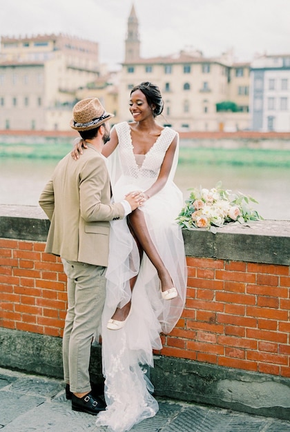 Lo sposo si trova vicino alla sposa seduta su un recinto di mattoni sulla riva del fiume