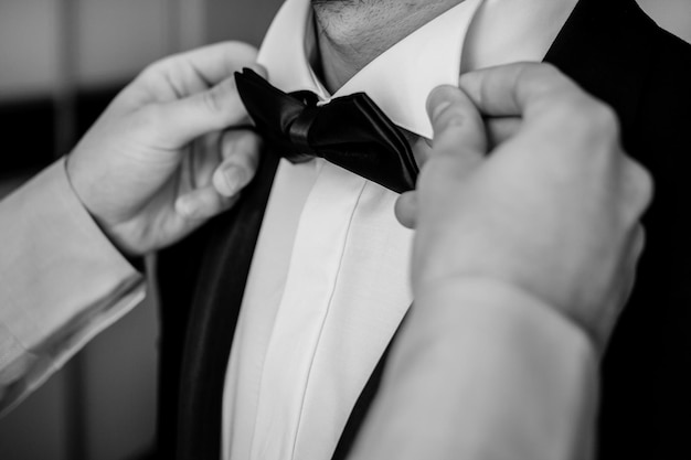 The groom straightens the bow tie. man straightening his black\
bow-tie. black and white photo