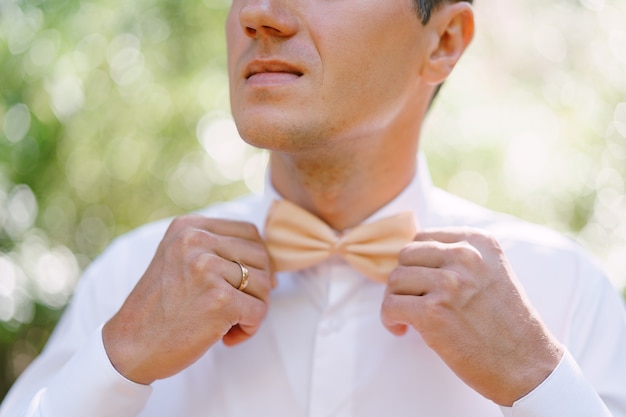 Groom straightens his bow tie on a white shirt closeup