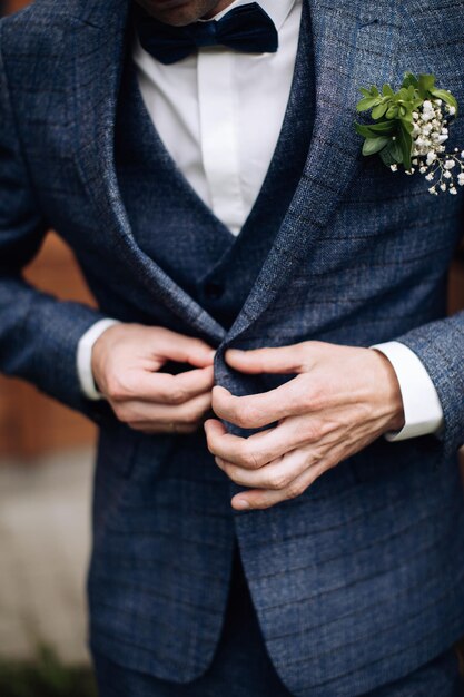 The groom in a suit adjusts the cuffs and fastens his\
jacket