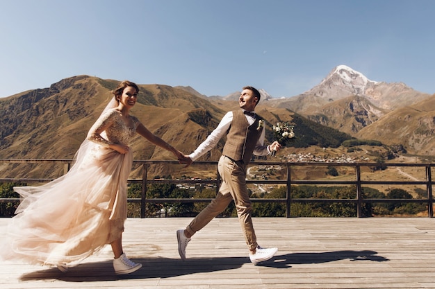 Groom in suit and bride in charming pink dress on the terasse with great mountain view