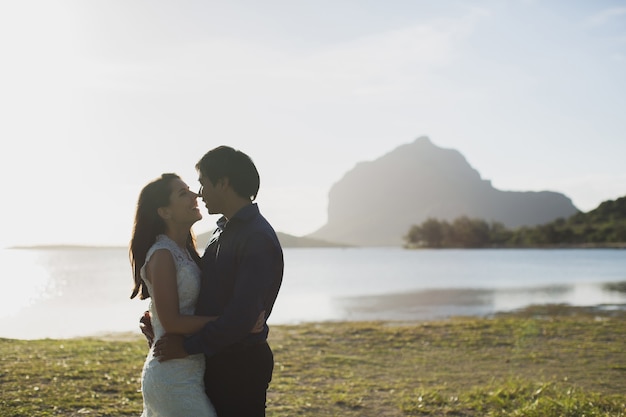 Groom in suit and the bride in a white dress standing on the shore of a mountain lake