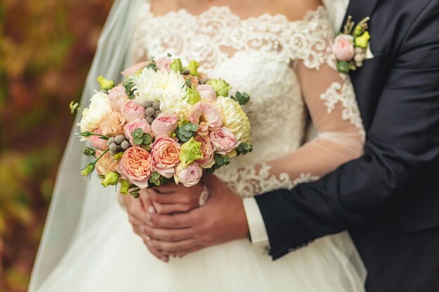 The groom in a suit and the bride in a white dress standing side by side and are holding bouquet