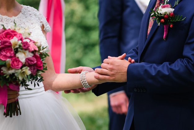 Groom in a suit holds the bride's hand in a white dress at the wedding