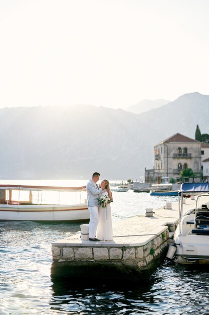 Foto lo sposo tocca il mento della sposa mentre è in piedi sul molo vicino alle barche ormeggiate