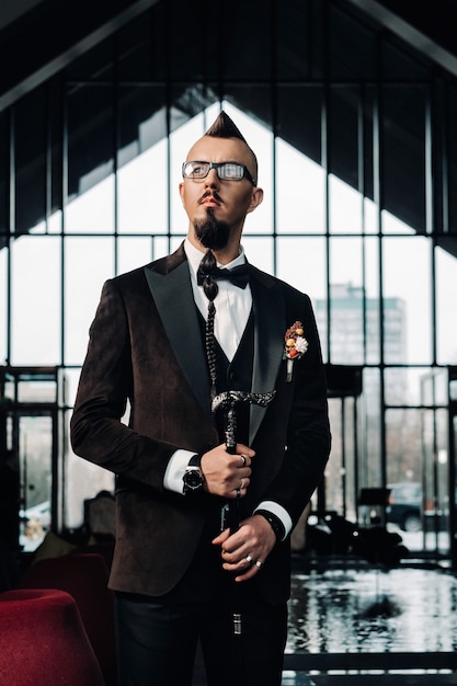 The groom in a tuxedo and bow tie with a mohawk hairstyle and a cane in the interior.