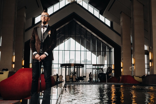 The groom in a tuxedo and bow tie with a mohawk hairstyle and a cane in the interior.