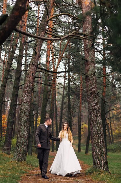 The groom in uniform holds bride hand in a wedding dress newlyw