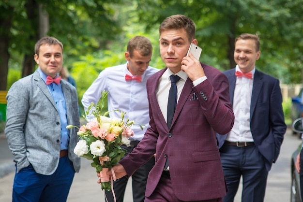 the groom walks with a bouquet and talks on the phone