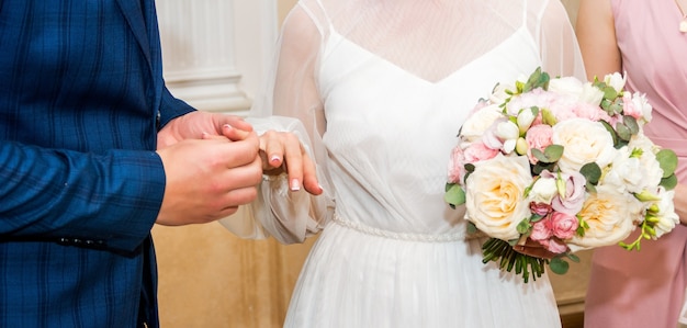 Groom wears bride a wedding ring Bride hand holds a beautiful wedding bouquet..