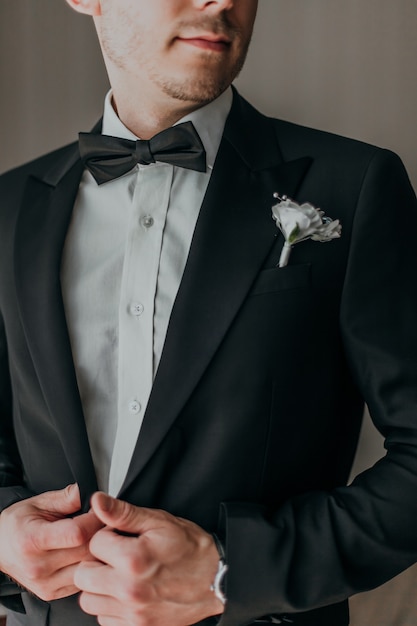 ホテルのホールで笑顔で花嫁を待っている結婚式の黒タキシードの新郎。衣装と蝶ネクタイのエレガントな新郎。
