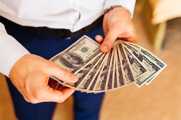 The groom in a white shirt and classic trousers holds a lot of money in his hands