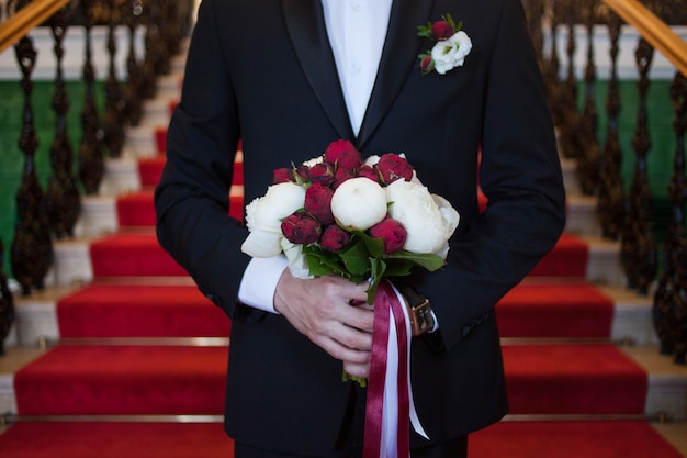 Lo sposo con il bouquet della sposa incontra la sua futura moglie, primo piano di peonie rosse e bianche