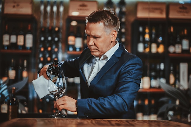 Groomed elegant wine sommelier is pooring red wine to the glass to taste it.