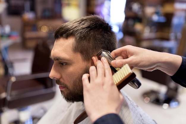 グルーミング、髪型、人のコンセプト – 理髪店で髪を切るトリマーを持つ男性と理髪師または美容師の手