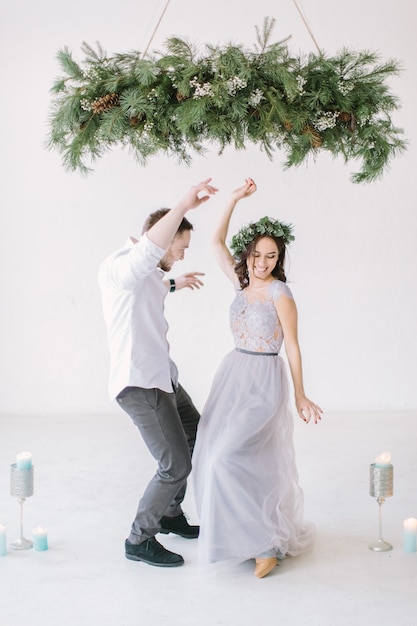 Groomsman and bridesmaid dressed in grey dress dancing in white room with wedding decorations