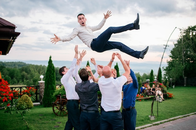 Groomsmen gooien vrolijke bruidegom staande op het gazon