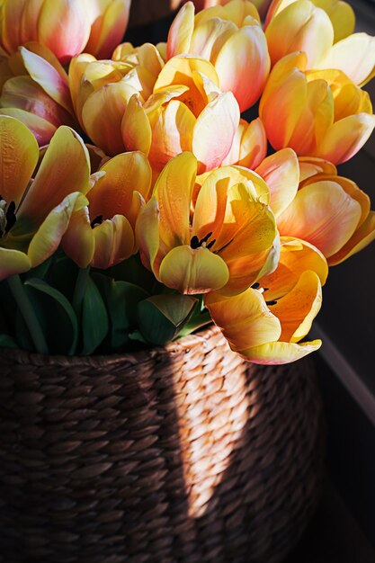 Groot boeket van geeloranje tulp bloemen in een waterhyacint mand in een witte moderne binnenkamer naast een groot raam op een zonnige zomerdag Floral home decor concept