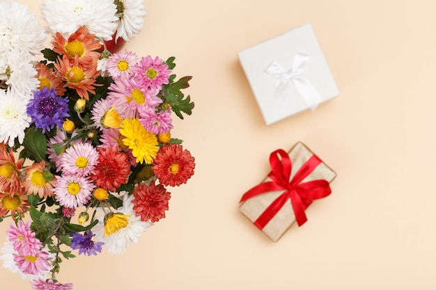 Groot boeket van kleurrijke verschillende bloemen en geschenk boxex op de beige achtergrond. Bovenaanzicht. Focus op bloemen.