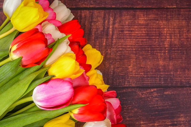 Groot helder boeket van veelkleurige tulpen op houten planken van donkerbruine kleur.