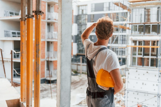 Groot project Jonge man aan het werk in uniform bij bouw overdag