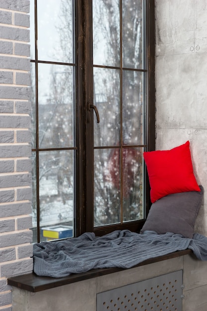 Groot raam met vensterbank met kussens en deken in de slaapkamer in loftstijl, buiten het raam sneeuw