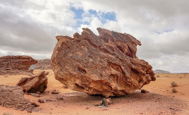 Groot rotsblok, zijkanten gevormd door erosie op oranje zand van de Wadi Rum-woestijn